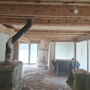 Démonstration d'un décapage par aérogommage sur des poutres en bois brut dans un intérieur en rénovation.